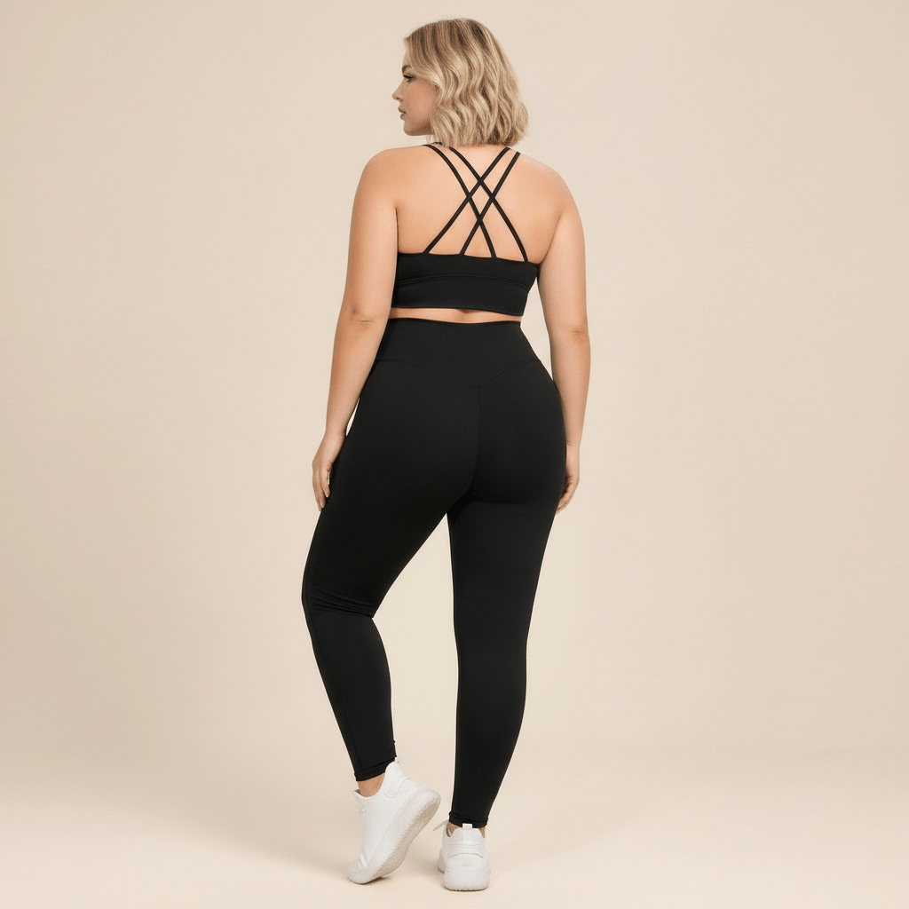 Vetement fitness femme grande taille noir, vue de dos, brassiere dos multi-bretelles croisees et legging taille haute, pose chic, fond studio beige.