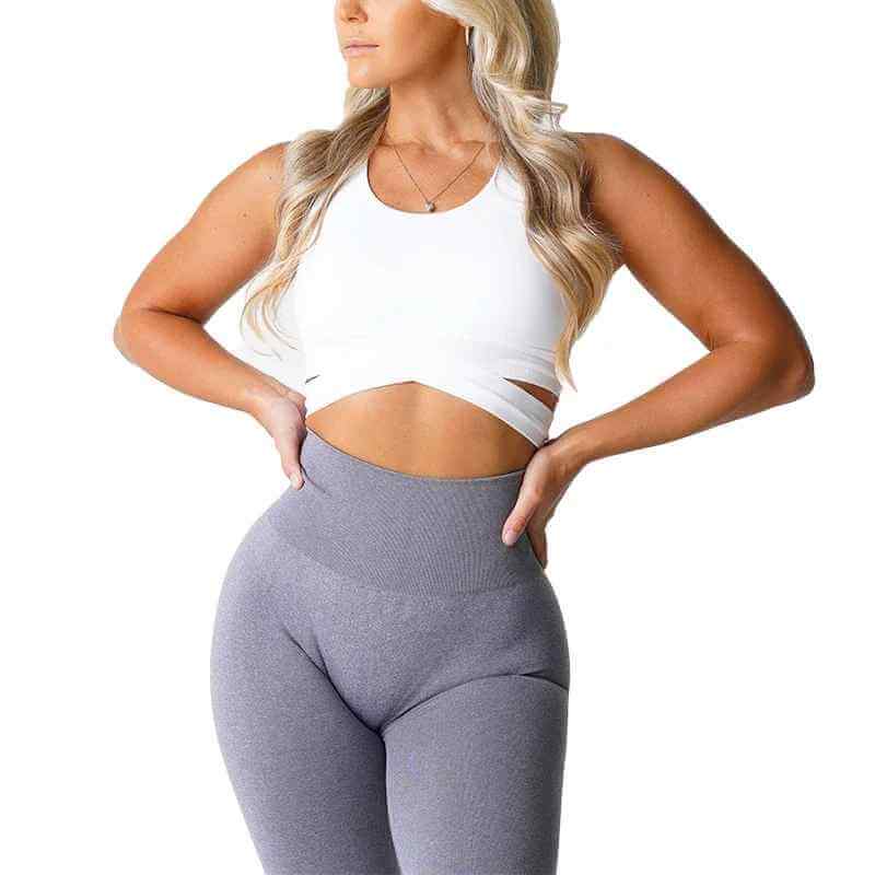 Brassière sport sans couture avec bretelles croisées, modèle taille XS-L, femme en haut blanc et leggings gris, pose confiante.