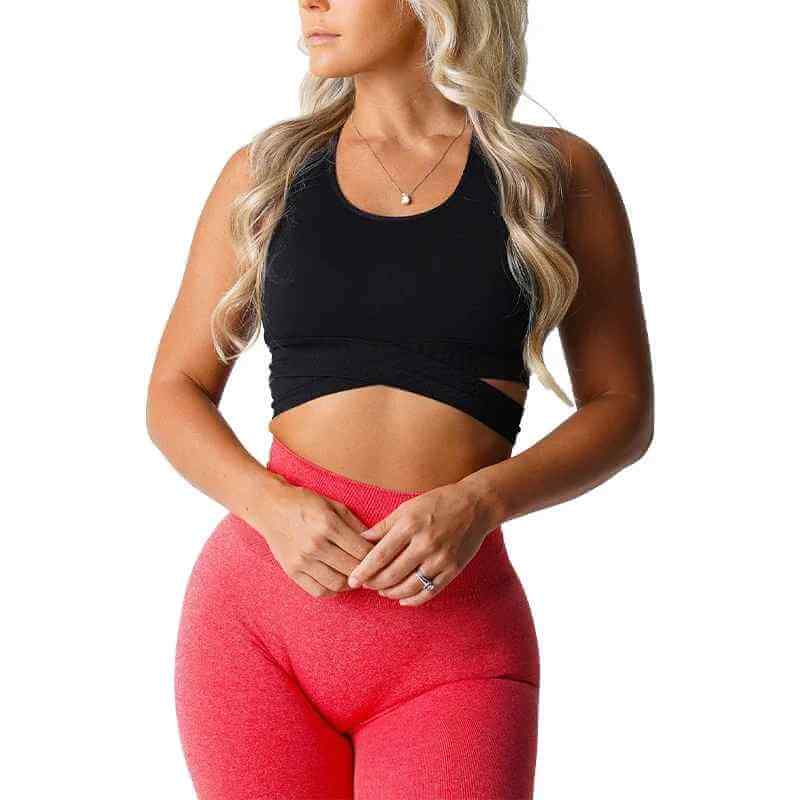 Brassière sport sans couture noir avec bretelles croisées, portée par une femme souriante en leggings rouges, style sportif.