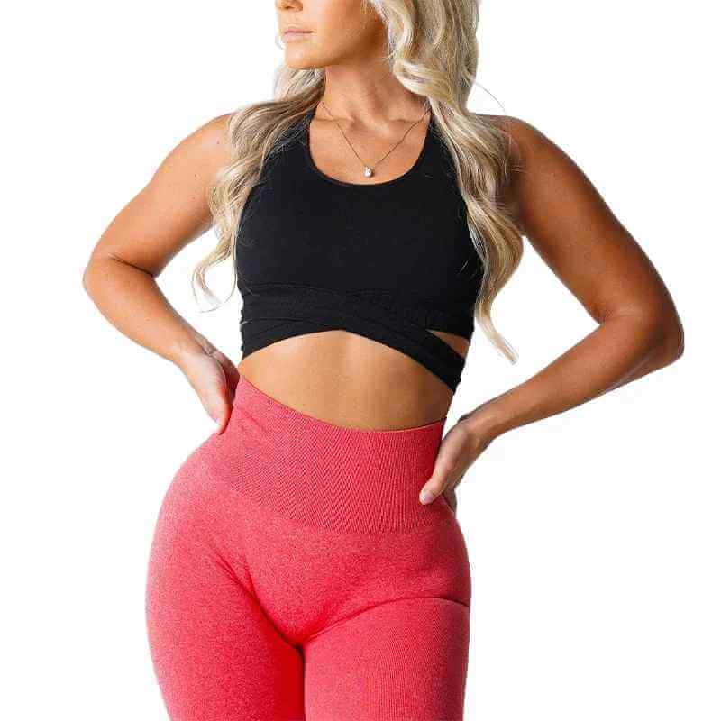 Brassière sport sans couture pour femme, noire, avec coupe croisée et Bretelles, portée par une femme athlétique en haut noir et leggings rouges.