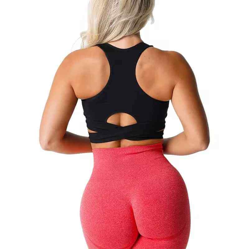 Brassière sport sans couture avec bretelles croisée portée par une femme, vue arrière, en haut noir et leggings rose vif.