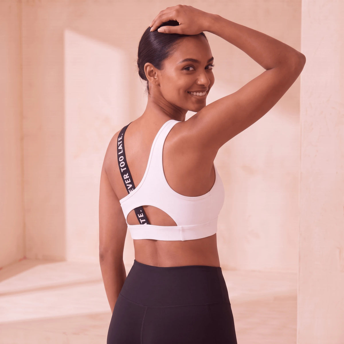 Brassière de sport blanche dos nu, regard souriant par-dessus l'épaule, découpe dans le dos