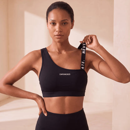 Brassière fitness noire de face, main qui tient la bretelle à message imprimée en blanc