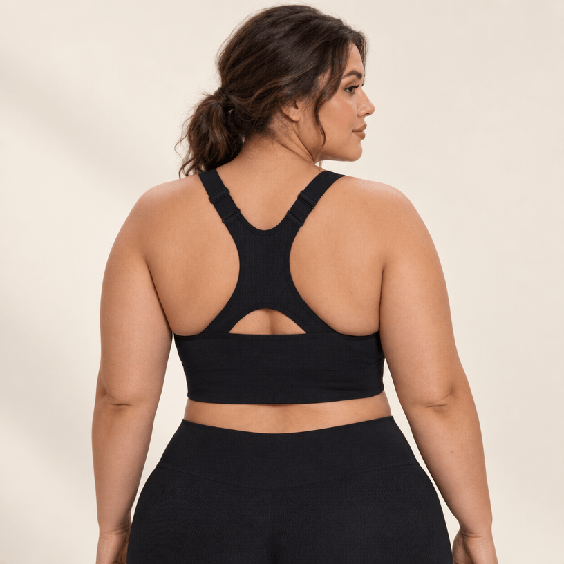 Dos nageur à découpe de la brassière running maintien fort noire, omoplates libres, studio fond ivoire.