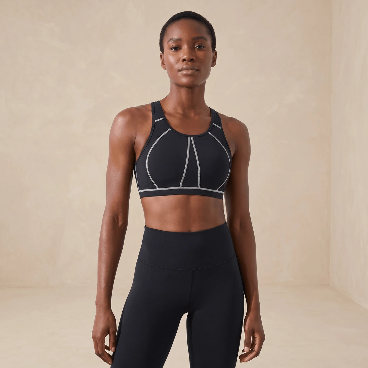 Brassière fitness noire à coutures blanches, dos nageur, portée de face avec un legging noir