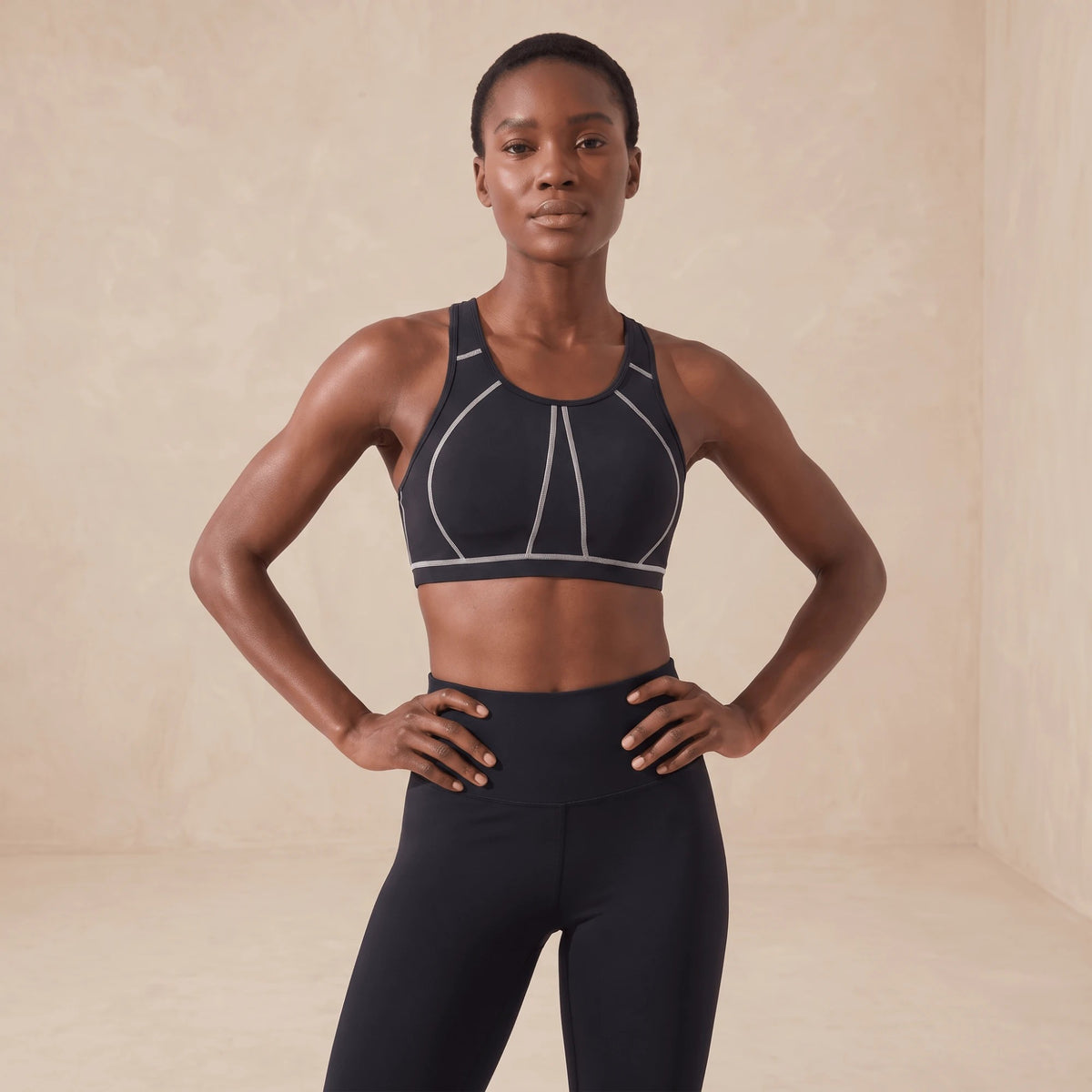 Brassière de sport noire portée mains sur les hanches, couverture complète et coutures blanches