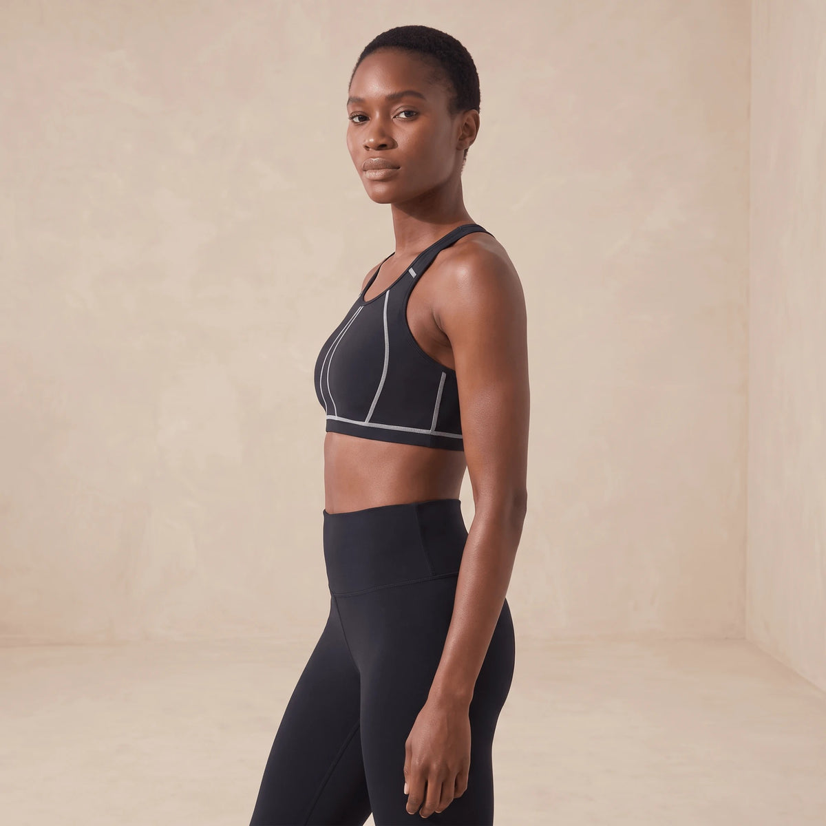 Brassière de sport noire sans armature vue de profil, encolure haute et coutures contrastées