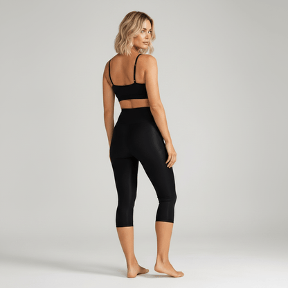 Femme vue de dos portant un collant anti cellulite noir, posture élégante, studio minimaliste ivory gray