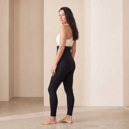Collant gainant ventre plat noir vu de dos en trois quarts, regard par-dessus l'épaule, ceinture haute