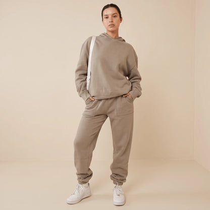 Ensemble sweat jogging femme taupe vu de face, mains dans les poches du pantalon, capuche et poignets côtelés