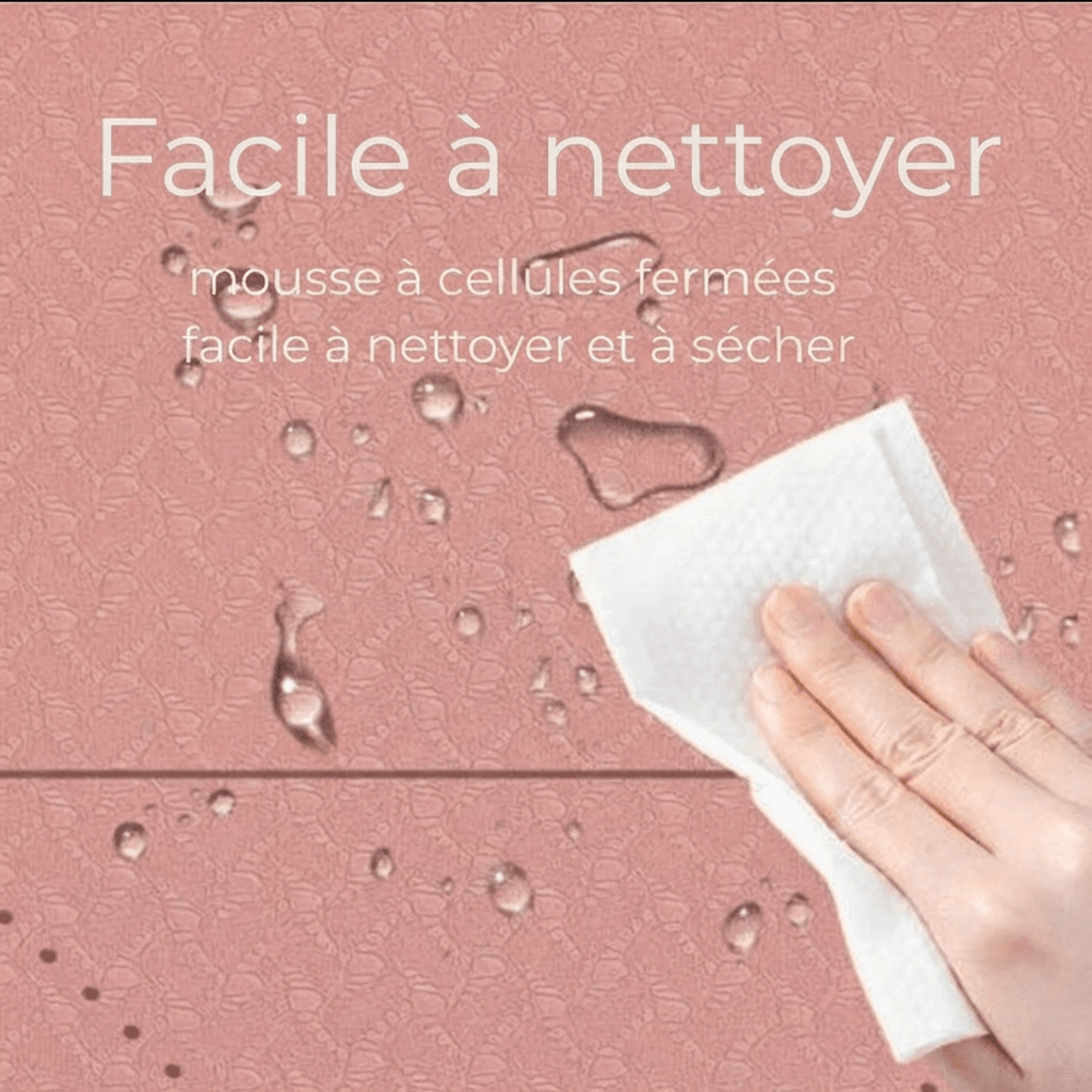 Gros plan du tapis Asana Aura rose poudré avec gouttes d’eau et main essuyant, texte “Facile à nettoyer – mousse à cellules fermées