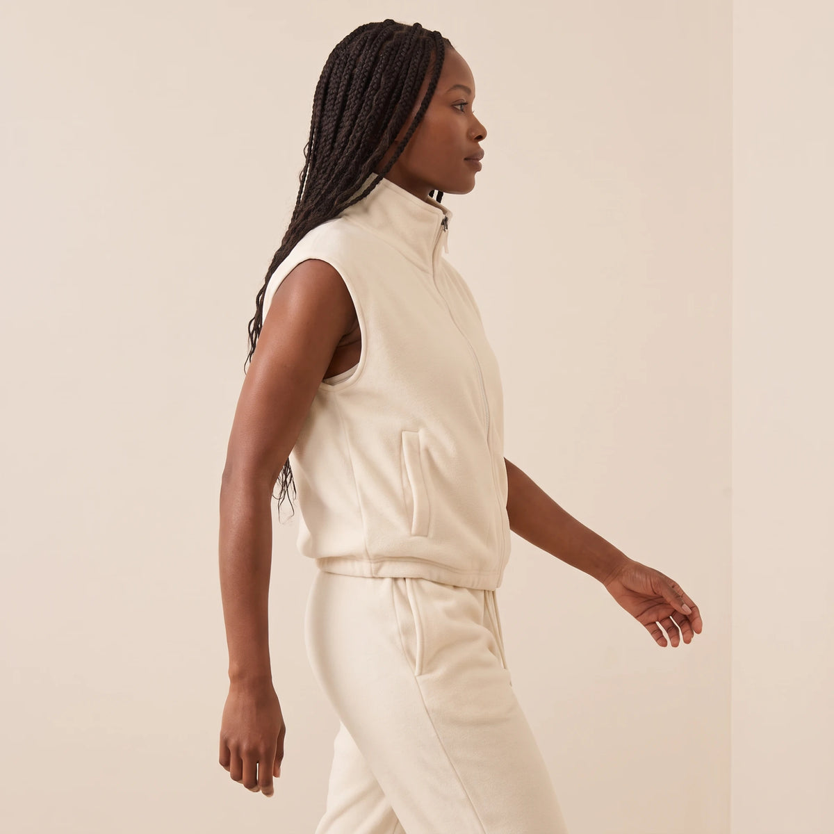 Gilet polaire femme blanc crème vu de profil en marche : poche latérale, emmanchure et ourlet resserré