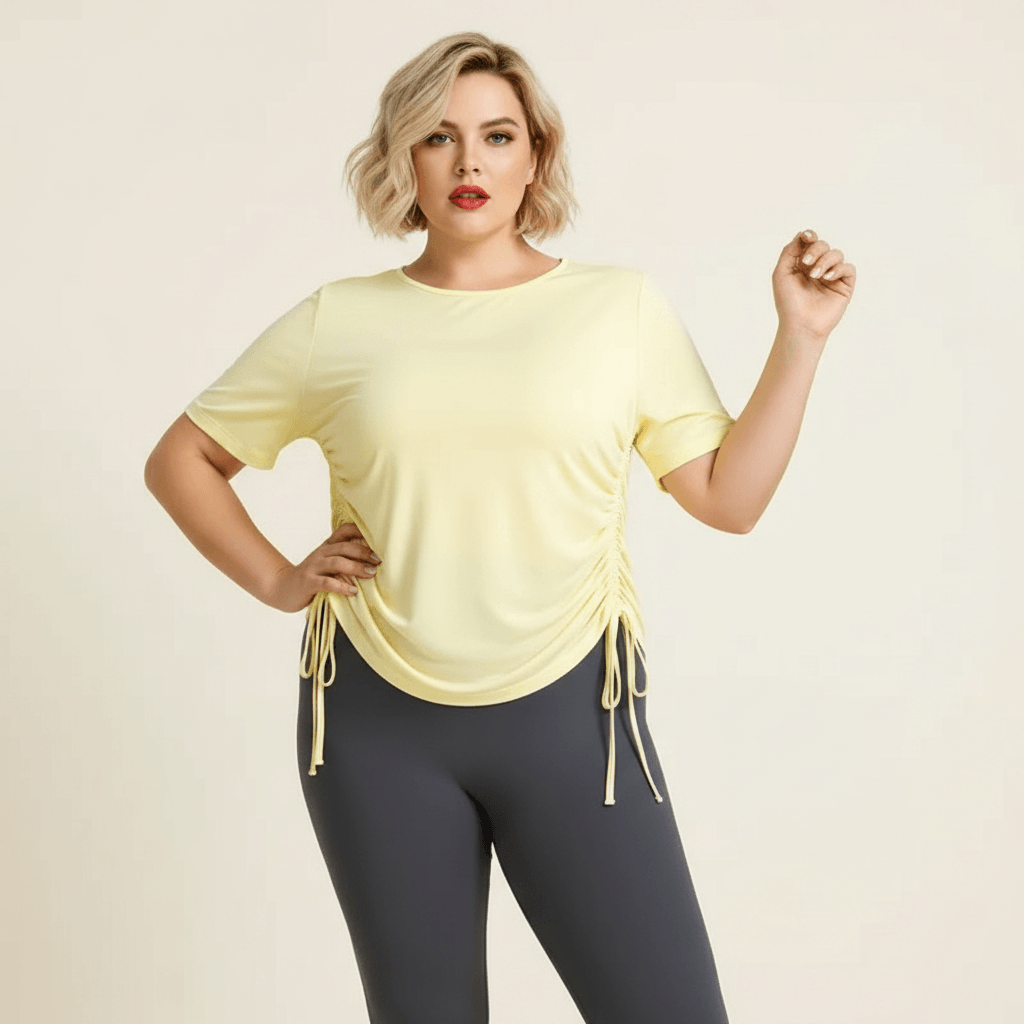 Haut de sport grande taille femme jaune pastel main tirant le cordon de serrage pose fashion sport fond studio crème