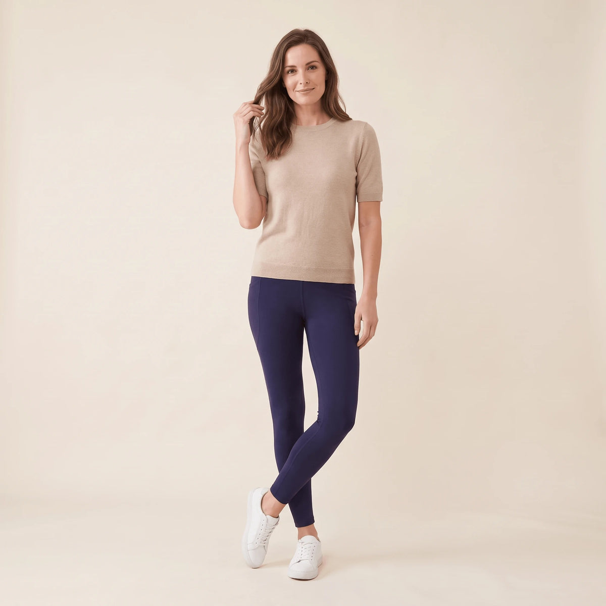 Legging avec poches marine porté avec un pull beige et des baskets blanches, jambes croisées