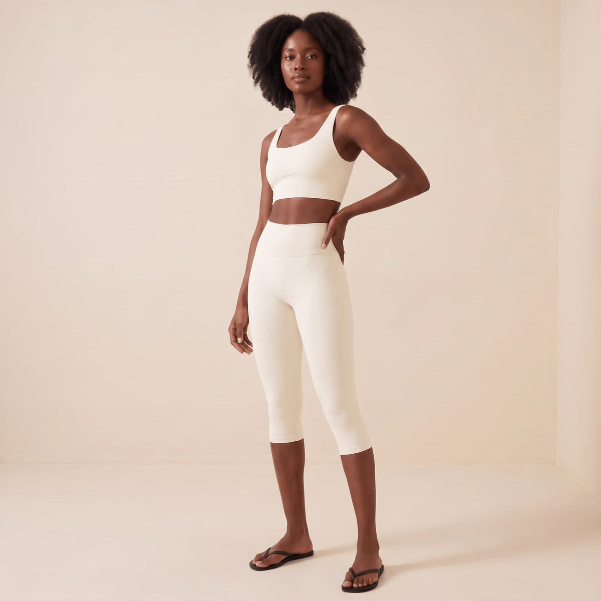 Legging capri blanc femme de trois quarts face, main sur la hanche : taille haute marquée et coupe ajustée tight fit