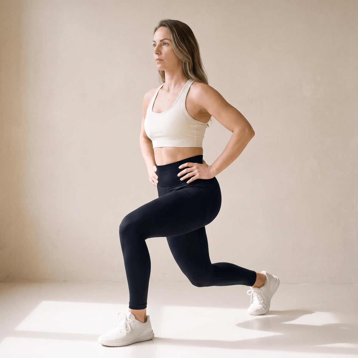 Legging fitness femme noir taille haute en fente avant pendant une séance de fitness, studio crème