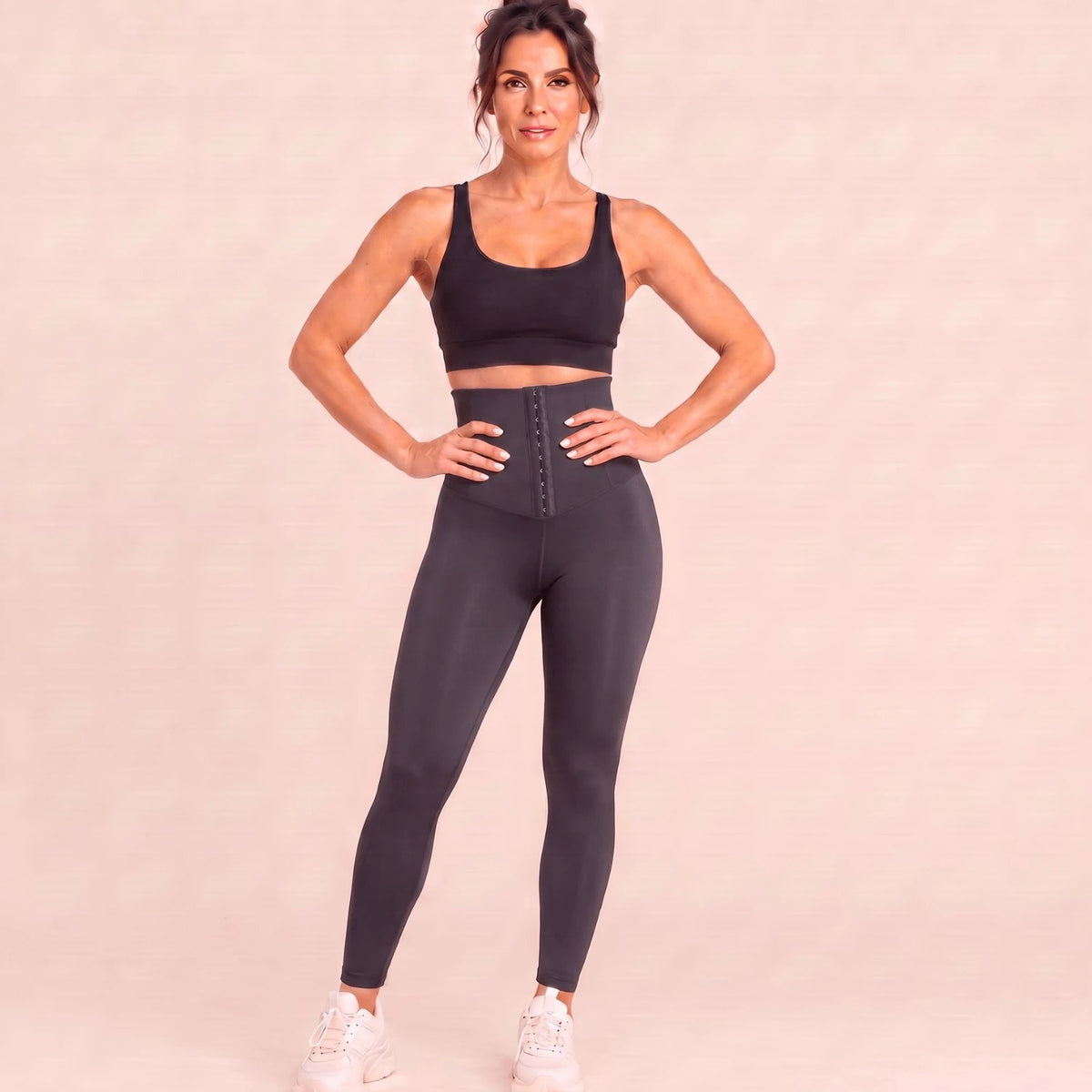 Legging gainant sport gris anthracite, mains sur les hanches : ceinture corset à crochets qui marque la taille et lisse le ventre