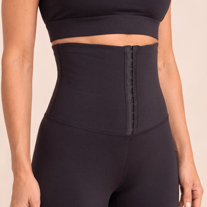 Détail de la ceinture corset d'un legging taille haute à crochets noir, de face : coutures plates et effet ventre plat