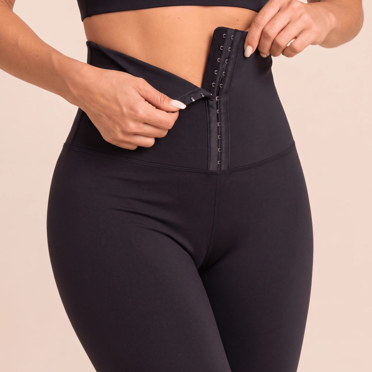 Gros plan sur la fermeture à crochets réglable d'un legging ceinture corset noir : on accroche les crochets au rang qui convient