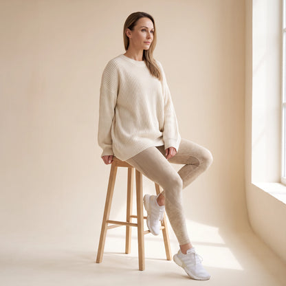 Legging galbant sans couture beige porté avec un grand pull crème, assise sur un tabouret en bois clair