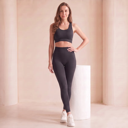 Legging noir taille haute sans couture, effet ventre plat, mannequin debout appuyée contre un socle blanc, main sur la hanche