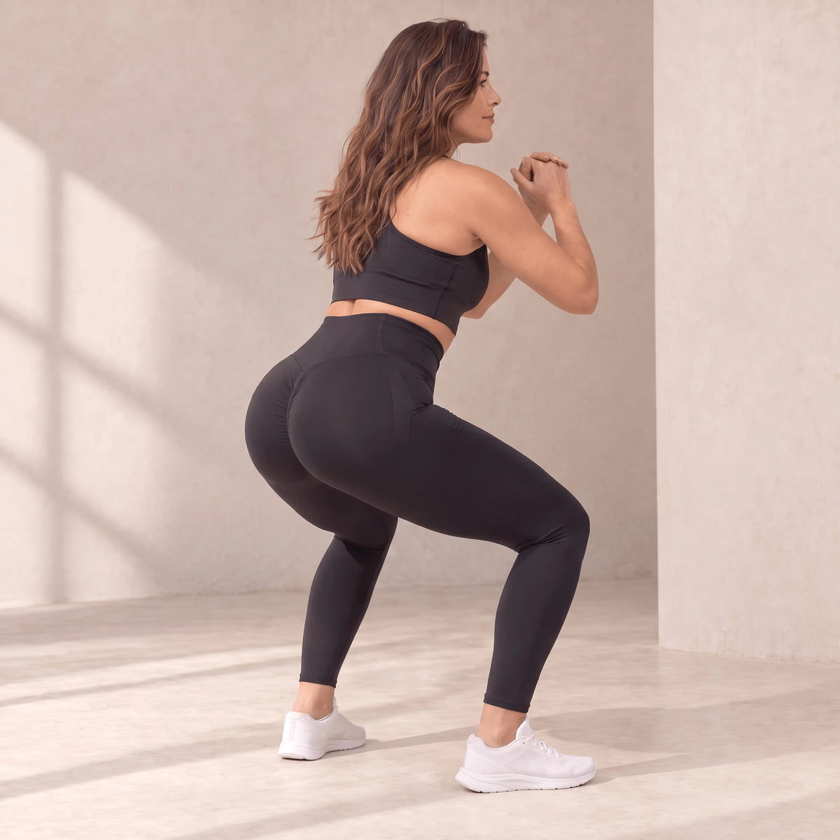 Legging sculptant noir en squat vu de dos, ceinture haute qui suit le mouvement, tissu extensible dans quatre directions