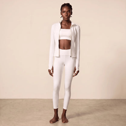 Legging sport blanc taille haute porté en tenue blanche complète avec veste zippée ouverte, brassière carrée, ceinture côtelée et longueur cheville
