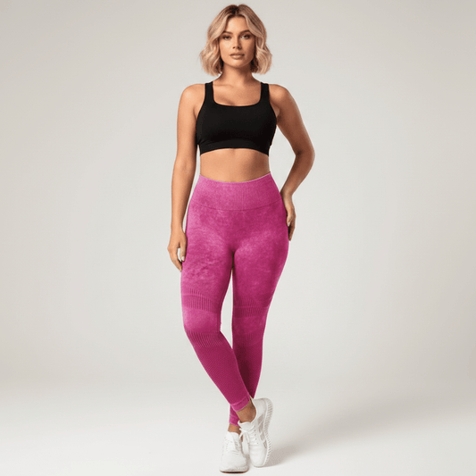 Legging Strong Push Up fuchsia/rose taille haute, vue de face pose élégante et confiante jambes légèrement croisées, maintien et compression visibles, brassière noire et baskets blanches, studio fond crème.