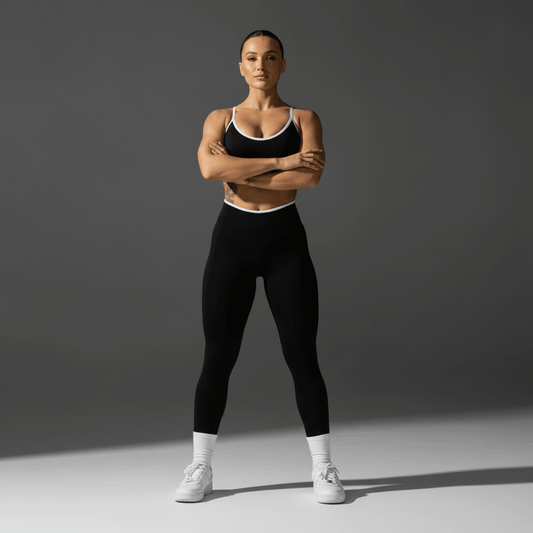 Homme ou femme athlète debout, bras croisés, portant leggings noirs et débardeur noir avec bordures blanches, baskets blanches. Produit: Push Up Leggings Sport.
