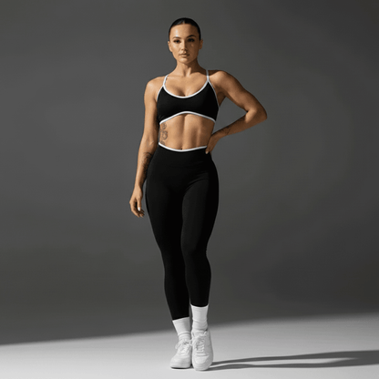Femme portant des leggings noirs et un crop top noir à bordures blanches, debout sur fond neutre, sneakers blancs. Alt: Push Up Leggings Sport : L'Élégance Dynamique au Service de Votre Performance.