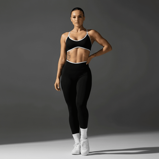 Femme portant des leggings noirs et un crop top noir à bordures blanches, debout sur fond neutre, sneakers blancs. Alt: Push Up Leggings Sport : L'Élégance Dynamique au Service de Votre Performance.
