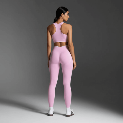 Femme vue de dos portant des leggings et un top de sport rose clair, look dynamique et élégant pour la performance.