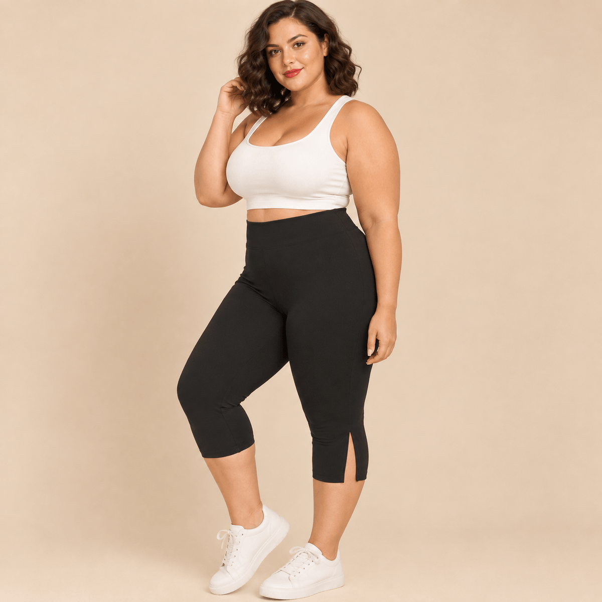 Short long sport femme grande taille noir capri compression taille haute avec empiècement vue de face trois-quarts main sur la hanche, pieds nus, fond studio crème
