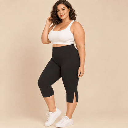 Short long sport femme grande taille noir capri compression taille haute avec empiècement vue de face trois-quarts main sur la hanche, pieds nus, fond studio crème