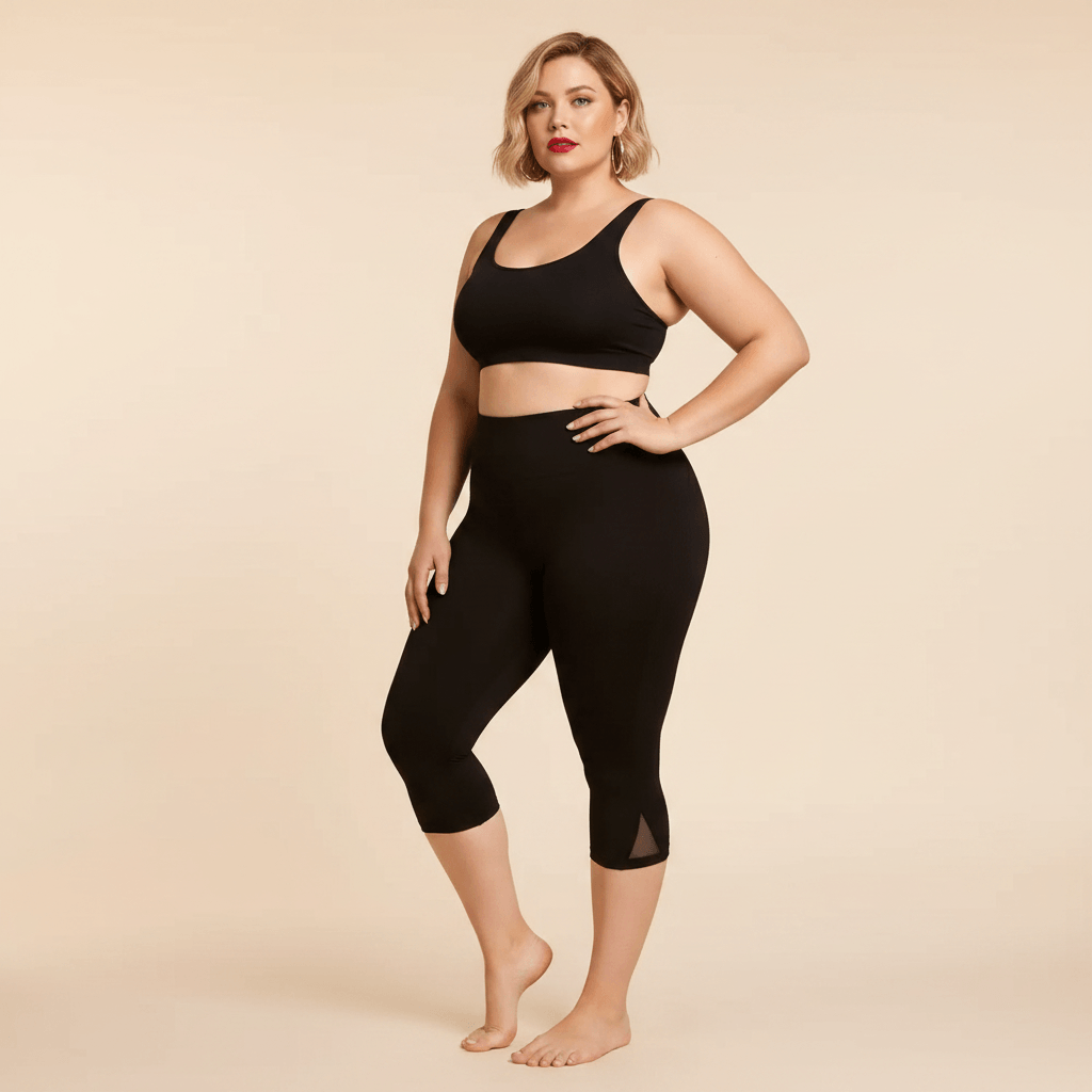 Short long sport femme grande taille noir capri compression taille haute avec empiècement mesh triangulaire sur le côté, vue de face trois-quarts main sur la hanche, pieds nus, fond studio crème