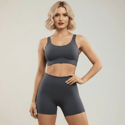 Shorty cargo gris taille haute vue de face debout – côtés lisses sans poche, ceinture haute gainante, brassière sport assortie, femme blonde carré wavy rouge à lèvres en studio ivoire