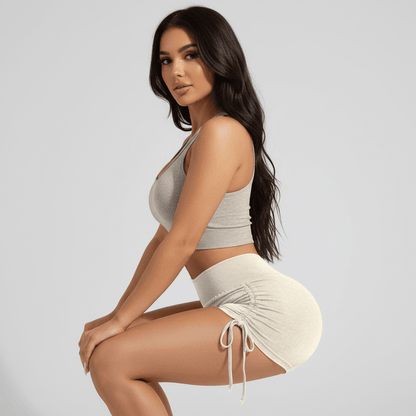 Femme sportive en chemise sans manches et short court gris, assise en profile, montrant une silhouette athlétique et respirante. Shorty fitness femme | Sculptant respirant.