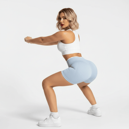 Sport short femme bleu ciel – pose squat dynamique côté, brassière blanche scrunch push-up