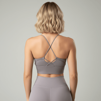 Brassière yoga hybride taupe, vue 3/4 dos, bretelles croisées, portée avec short gris taille haute, studio minimaliste gris clair.