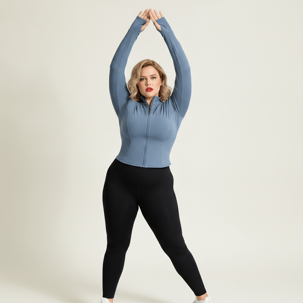 Veste de sport grande taille femme bleu-gris zippée avec trous pouces, col montant, bras levés pour montrer l’extensibilité et les manches, legging noir.